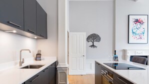 A modern kitchen with dark grey cabinets, white countertops, and a central white door. - JOIVY York Place Apartment in Georgian City Centre Building (Edinburgh)