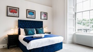 A bedroom with a large bed, two nightstands, a window with a view, and three framed pictures on the wall. - JOIVY York Place Apartment in Georgian City Centre Building (Edinburgh)