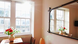 A room with a large window, a mirror, a table with a vase of flowers, and a chair. - JOIVY Bright New Town 2 bed Apt - 5 Mins to Princes St (Edinburgh)