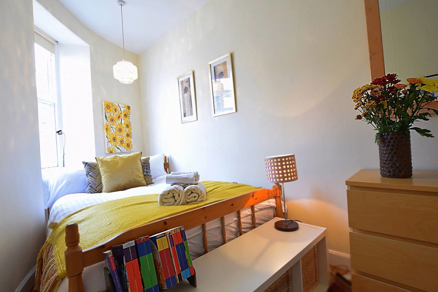 A bedroom with a bed, bedside table, lamp, dresser, and a window.