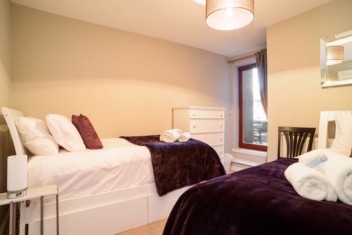 A bedroom with two beds, a dresser, a chair, and a window with curtains.