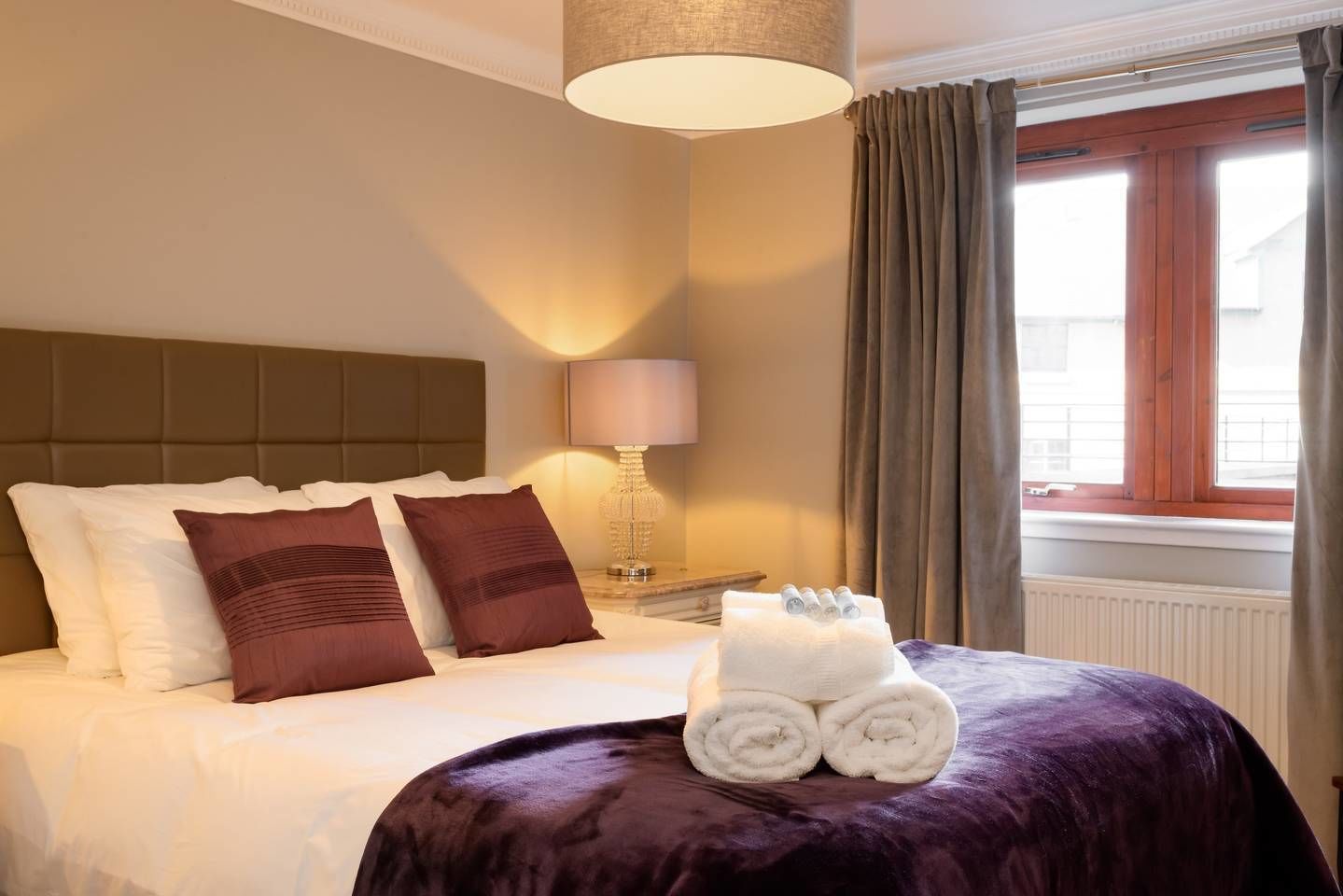 A hotel room with a large bed, a nightstand with a lamp, and a window with curtains.