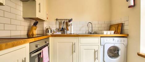 A compact kitchen with a washing machine, wooden countertops, and a tiled backsplash.