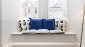A white paneled bench with a window seat, featuring a pineapple-patterned pillow and a solid blue pillow. - JOIVY Iconic Cockburn Street 4 Bedroom Apartment: Heart of Old Town (Edinburgh)