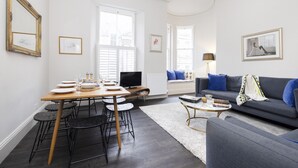 A modern living room with a dining area, featuring a sofa, coffee table, and a TV. - JOIVY Iconic Cockburn Street 4 Bedroom Apartment: Heart of Old Town (Edinburgh)