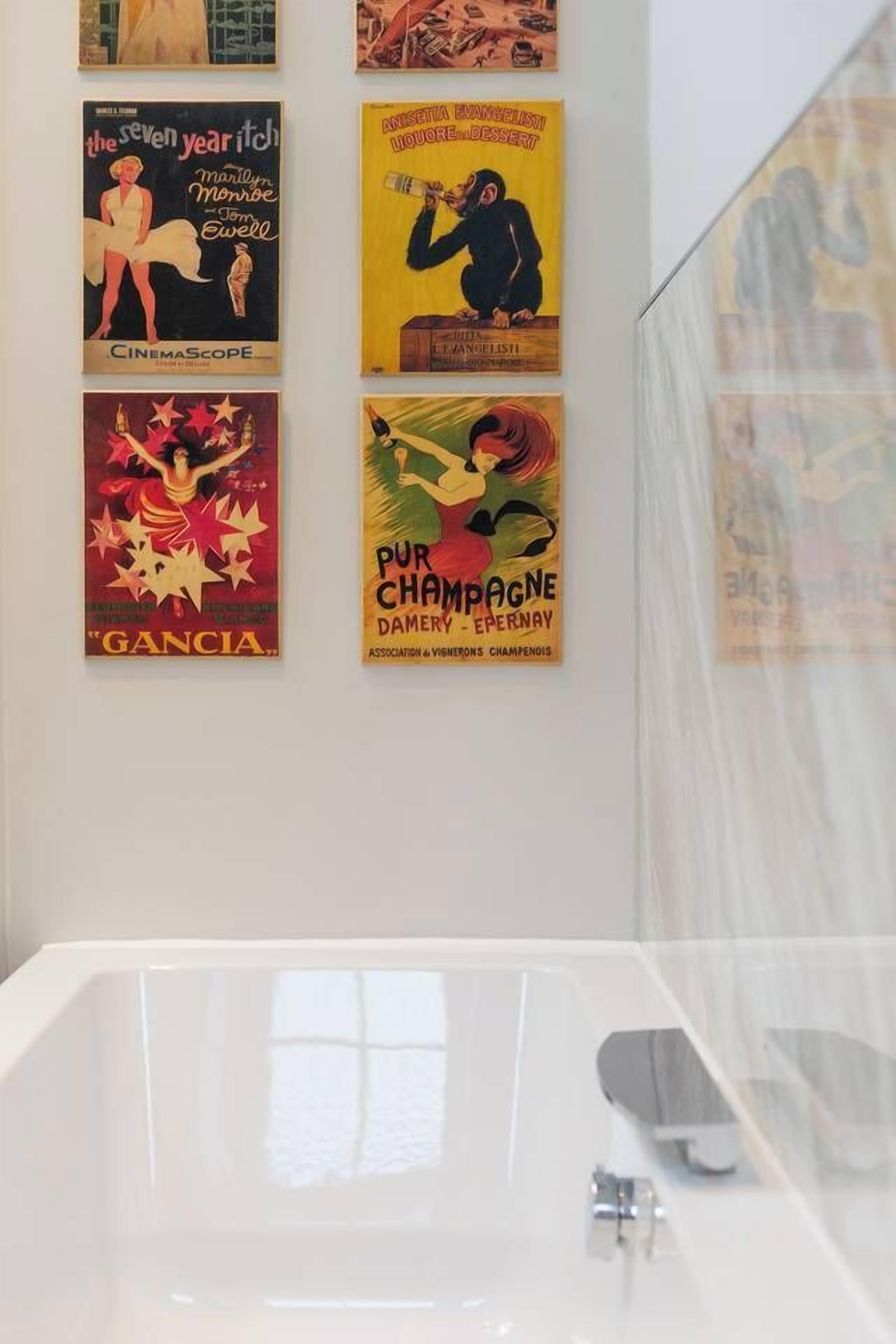 A bathroom with a white bathtub, a mirror, and vintage movie posters on the wall.