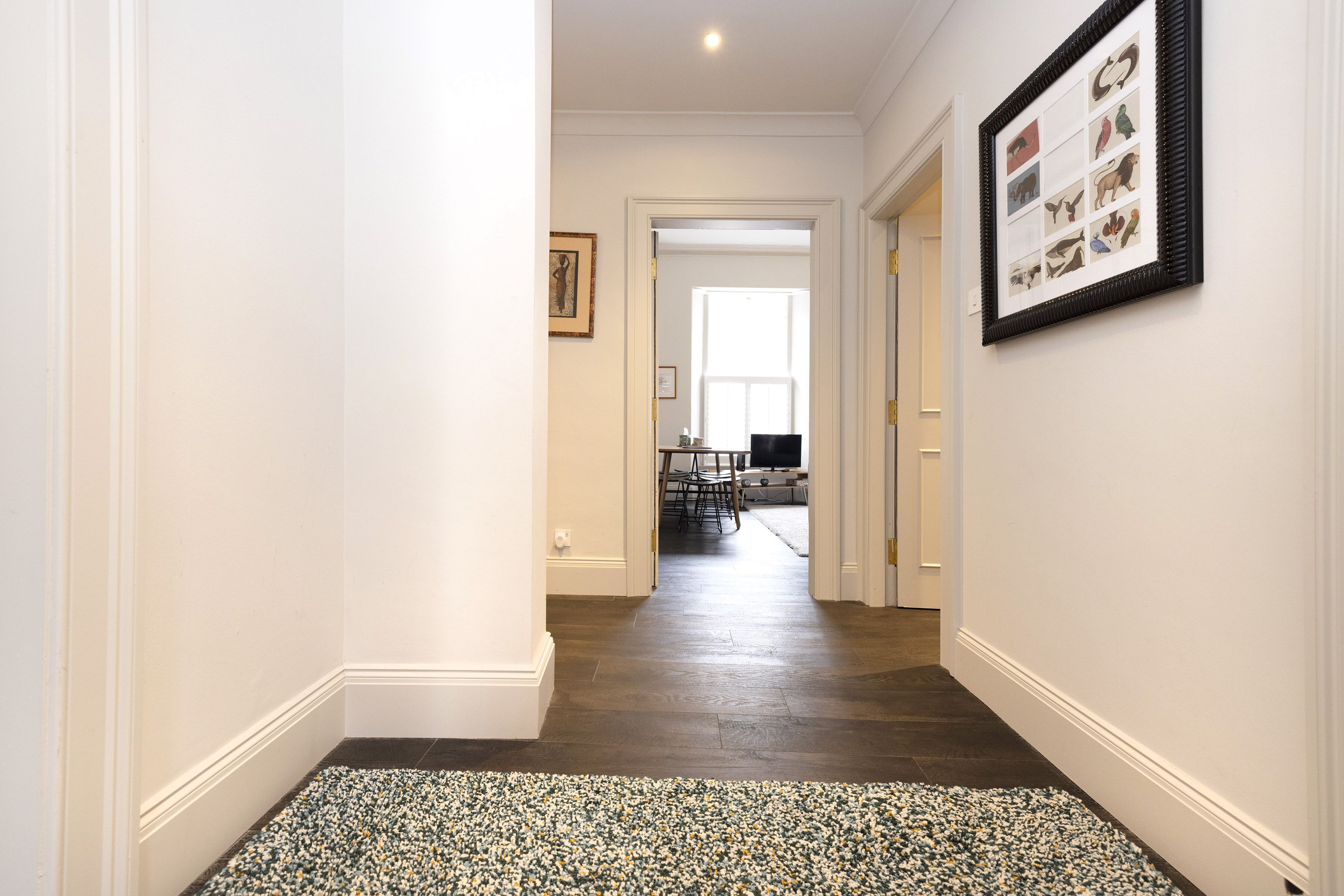 Un couloir avec un tapis à motifs, un tableau encadré au mur et, au fond, un coin repas.