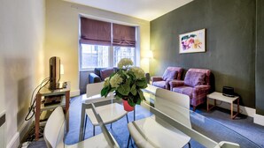 A hotel room with a dining table, two chairs, a sofa, a small side table, and a lamp. - JOIVY Perfect Location! - Stylish & Cosy Rose St Apt (Edinburgh)