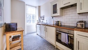 A kitchen with white cabinets, a wooden countertop, a microwave, a toaster, and a window with blinds. - JOIVY Perfect Location! - Stylish & Cosy Rose St Apt (Edinburgh)