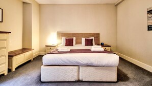 A double bed with a wooden headboard, two bedside tables, a nightstand, and a wall-mounted clock. - JOIVY Perfect Location! - Stylish & Cosy Rose St Apt (Edinburgh)