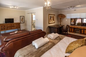 A hotel room with a sofa, a bed with a fur throw, a desk with a chair, a television, and artwork on the walls. - Antiqua Guest House (George)