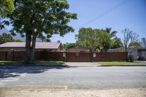 A gated property with a large tree in the foreground, a building with a red roof, and a clear blue sky. - Antiqua Guest House (George)