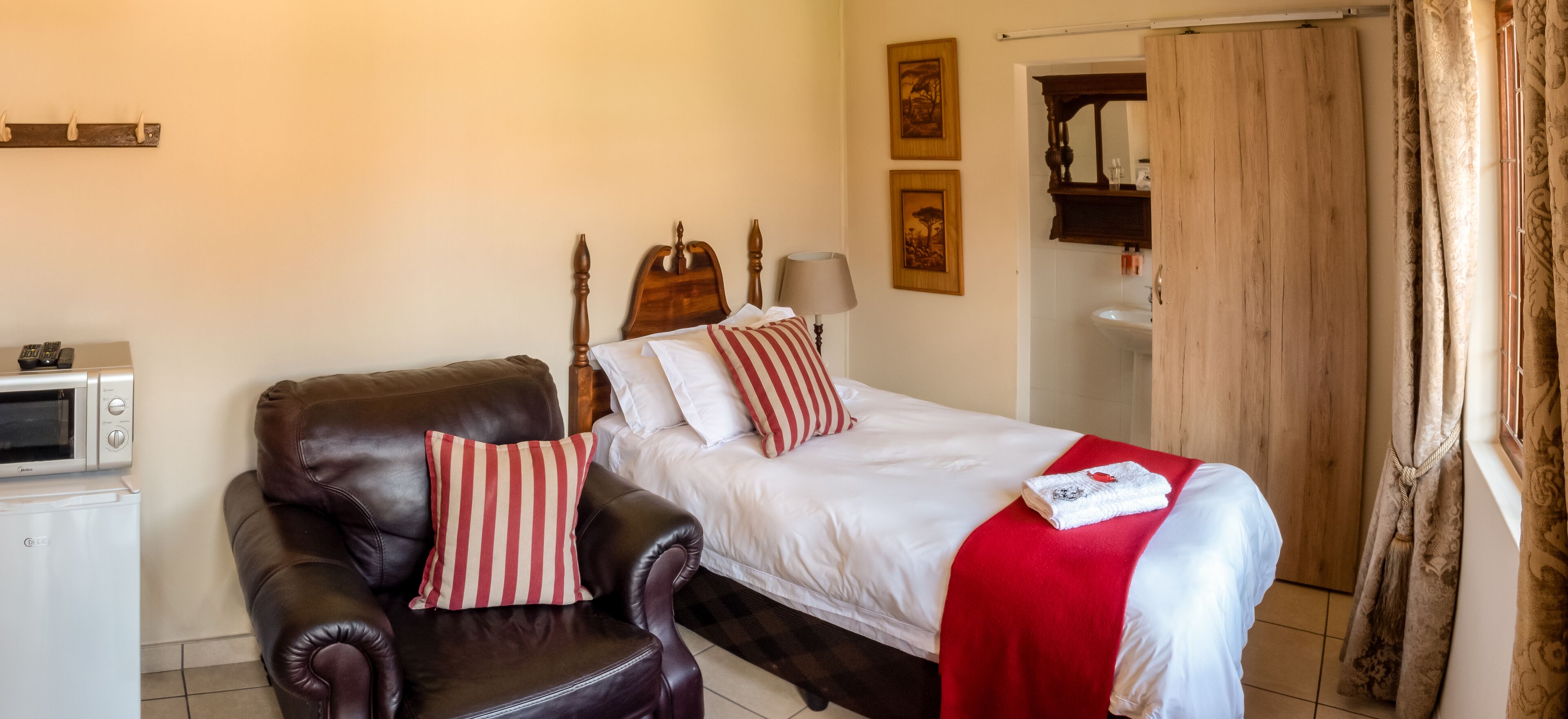 A hotel room with a bed, a leather armchair, a microwave, and a sink.