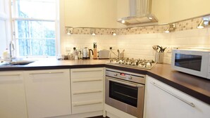 Una cocina moderna con armarios blancos, estufa a gas, horno, microondas y un ventanal que proporciona luz natural.