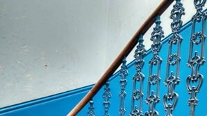 Una escalera con barandillas de metal ornamentadas y una pared azul.