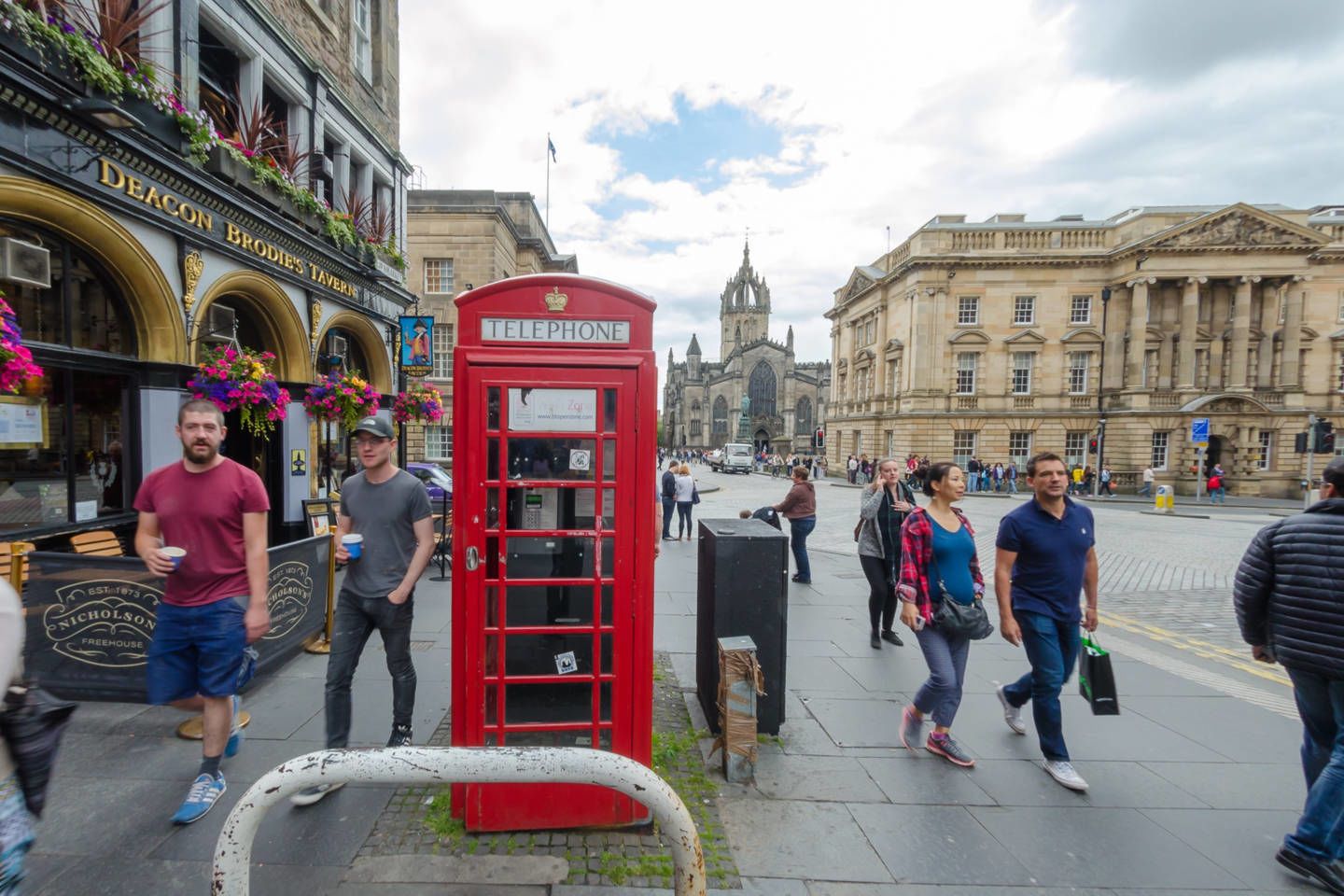 A red British telephone booth on a city street with historic buildings in the background.
