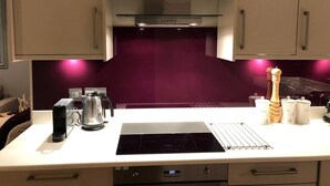Een moderne keuken met een roestvrijstalen afzuigkap, een zwart inductiekookveld, een waterkoker, een koffiezetapparaat en een set zout- en pepervaatjes.