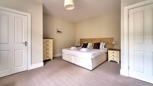 Une chambre à coucher comprenant un lit, des tables de chevet, une commode et un luminaire suspendu.