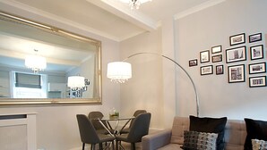 Een moderne woonkamer met een eethoek, een grote spiegel, een kroonluchter en een wand met ingelijste foto's.