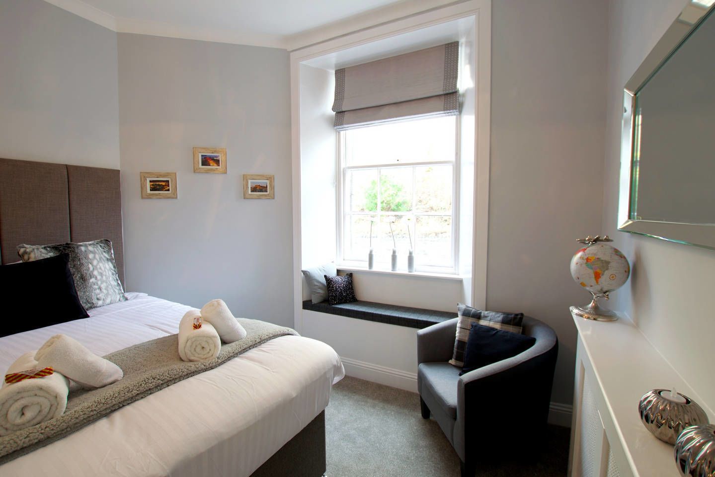 A hotel room with a bed, a window seat, a small table, and a globe on the wall.