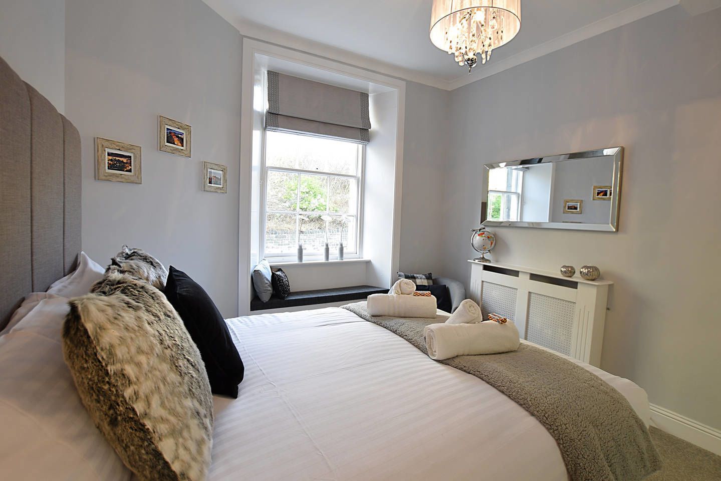 A modern bedroom with a large bed, a bedside table, a mirror, and a window with a view.