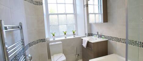 A bathroom with a toilet, sink, and bathtub. There is a window above the toilet, and a mirror above the sink.