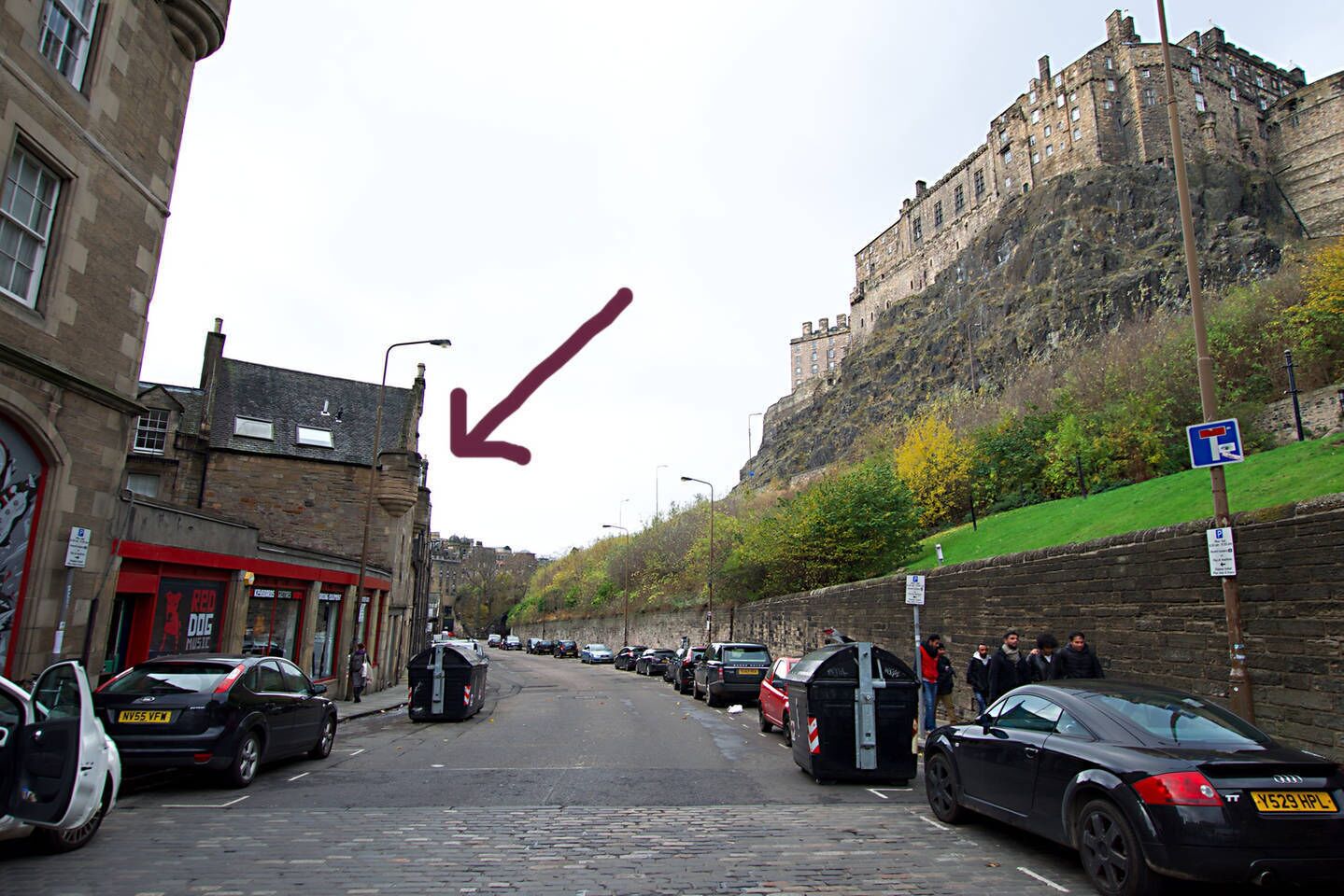 Eine Straße mit parkenden Autos, ein schlossartiges Gebäude auf einem Hügel und ein rotes DSO-Schild.