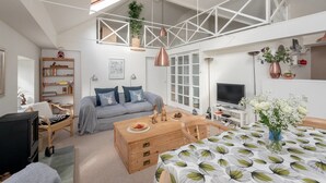 Un salon moderne avec un canapé gris, une table basse en bois et un coin repas agrémenté d’une nappe à motifs.
