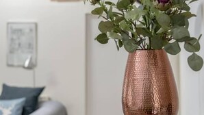 Une pièce comprenant un lit, une petite table ornée d’un vase en cuivre et d’une plante succulente, ainsi qu’un mur agrémenté d’un luminaire au design géométrique.