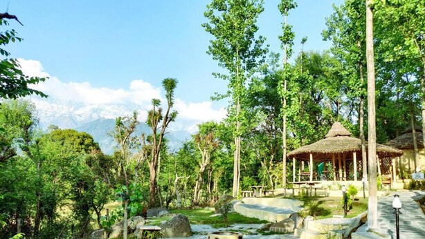 A natural setting with a thatched-roof pavilion, stone pathways, and lush greenery. - Dev Bhoomi Farms & Cottages (Dharamshala)