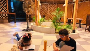 A child and an adult reading in a room with a checkered floor, a fan, and plants. - Dev Bhoomi Farms & Cottages (Dharamshala)