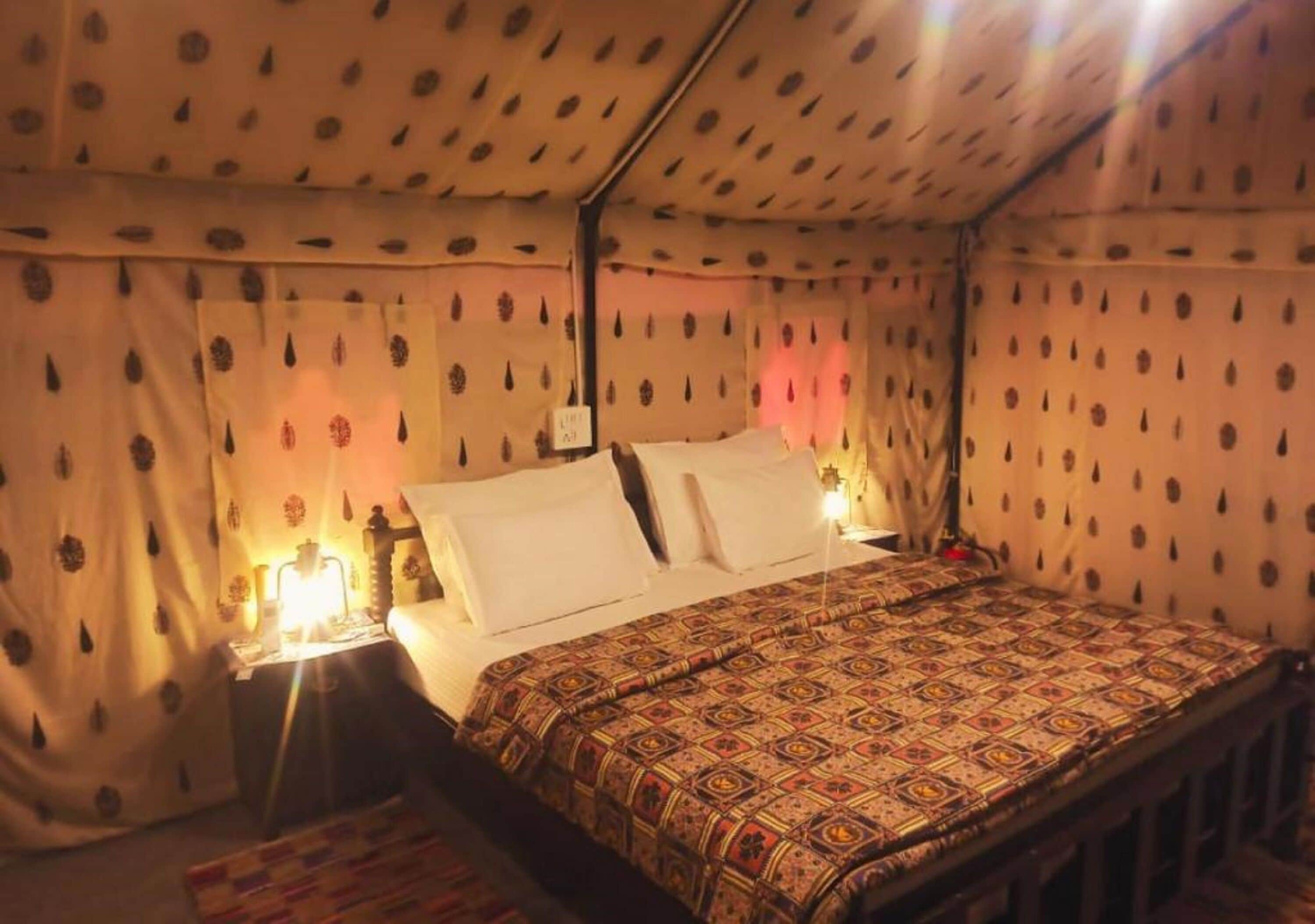 A single bed with a patterned bedspread, a nightstand with a lamp, and curtains with a leaf pattern.
