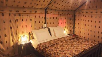 A single bed with a patterned bedspread, a nightstand with a lamp, and curtains with a leaf pattern.