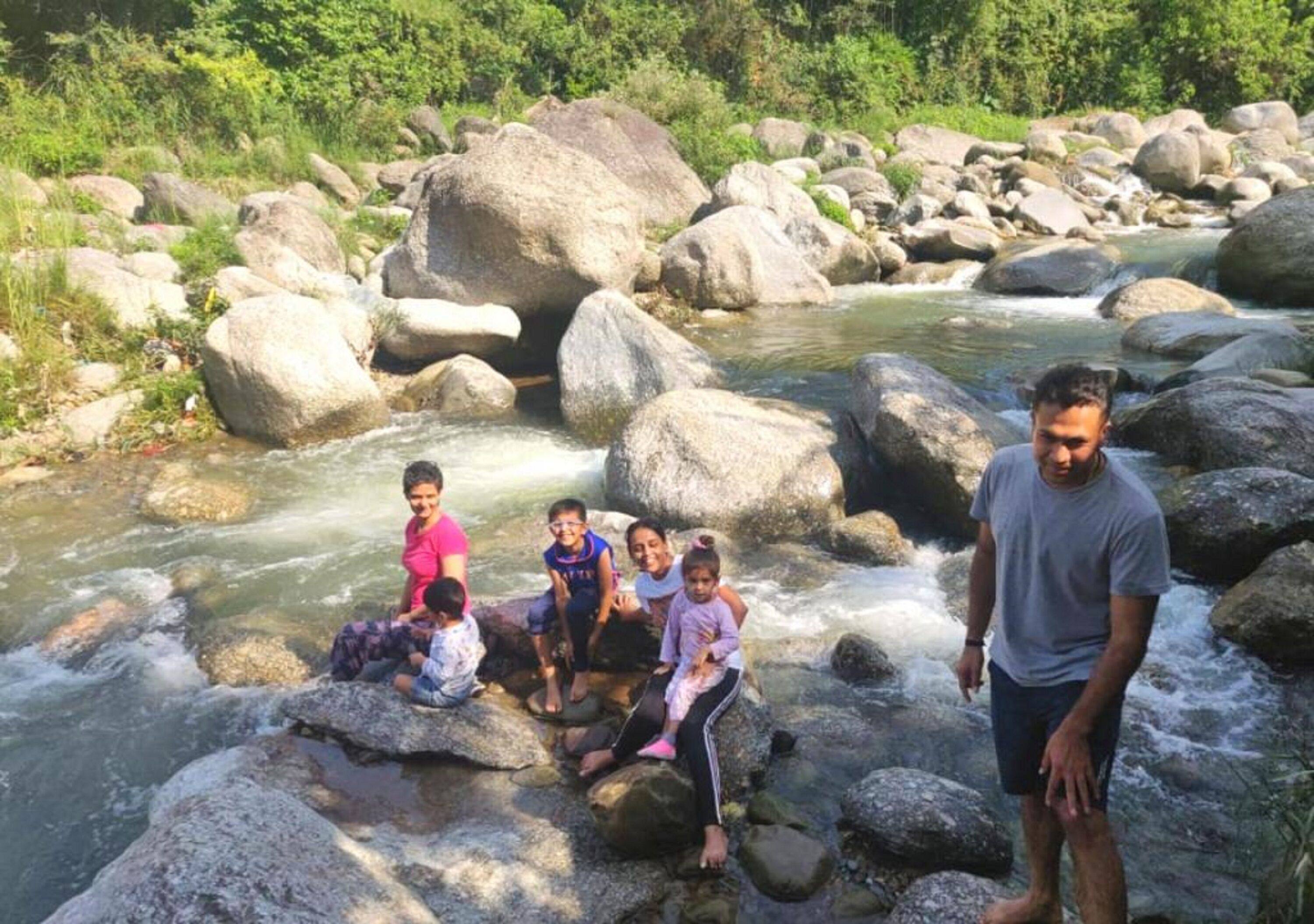 Um grupo de pessoas sentadas em rochas perto de um rio corrente, cercado por grandes pedras e vegetação.