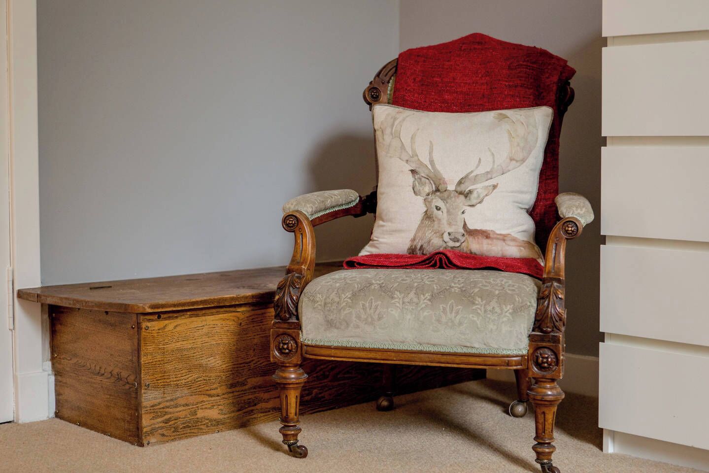 Een houten stoel met een kussen met een hertenprint, geplaatst naast een houten dressoir.