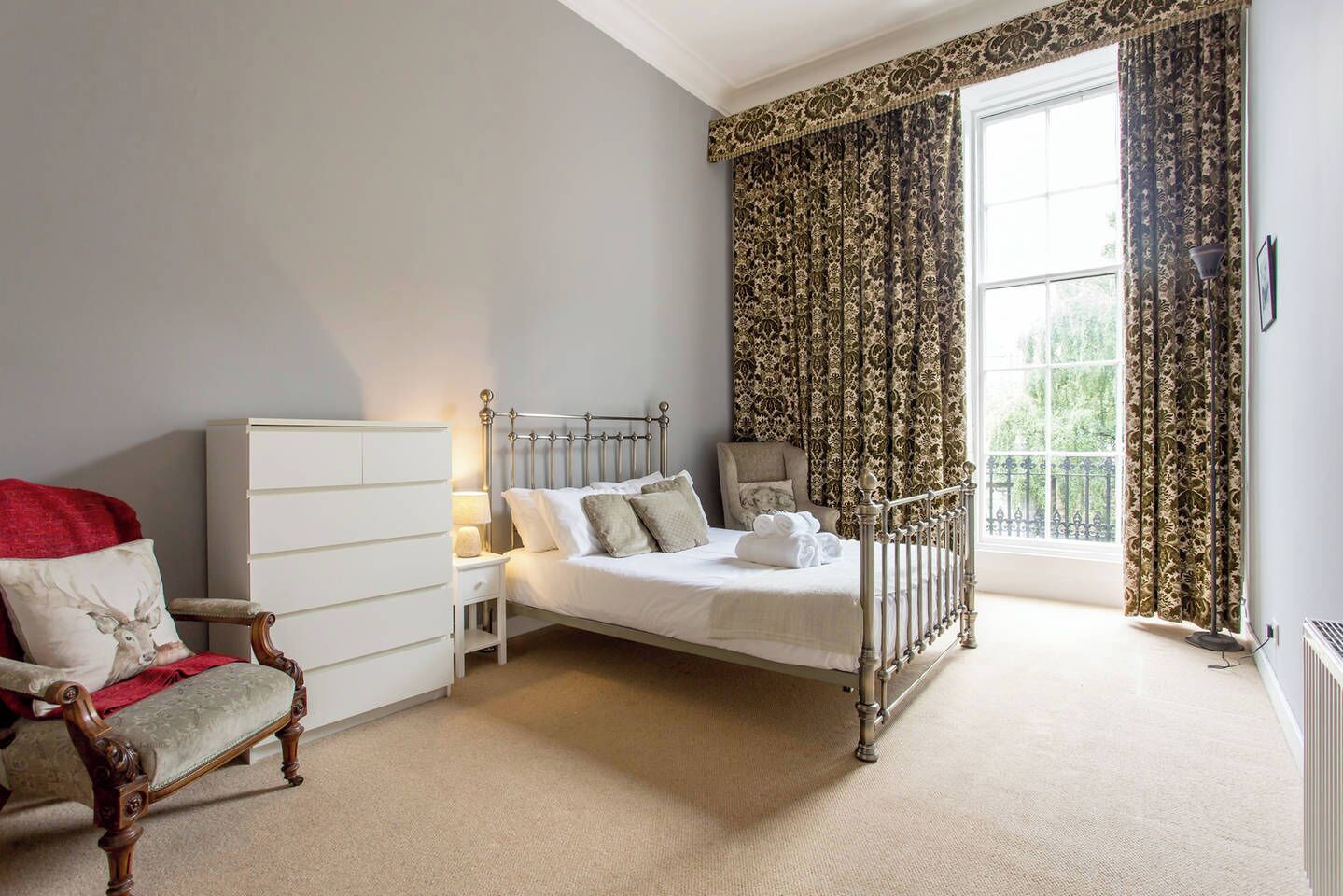 A bedroom with a bed, a chair, a dresser, and a window with curtains.