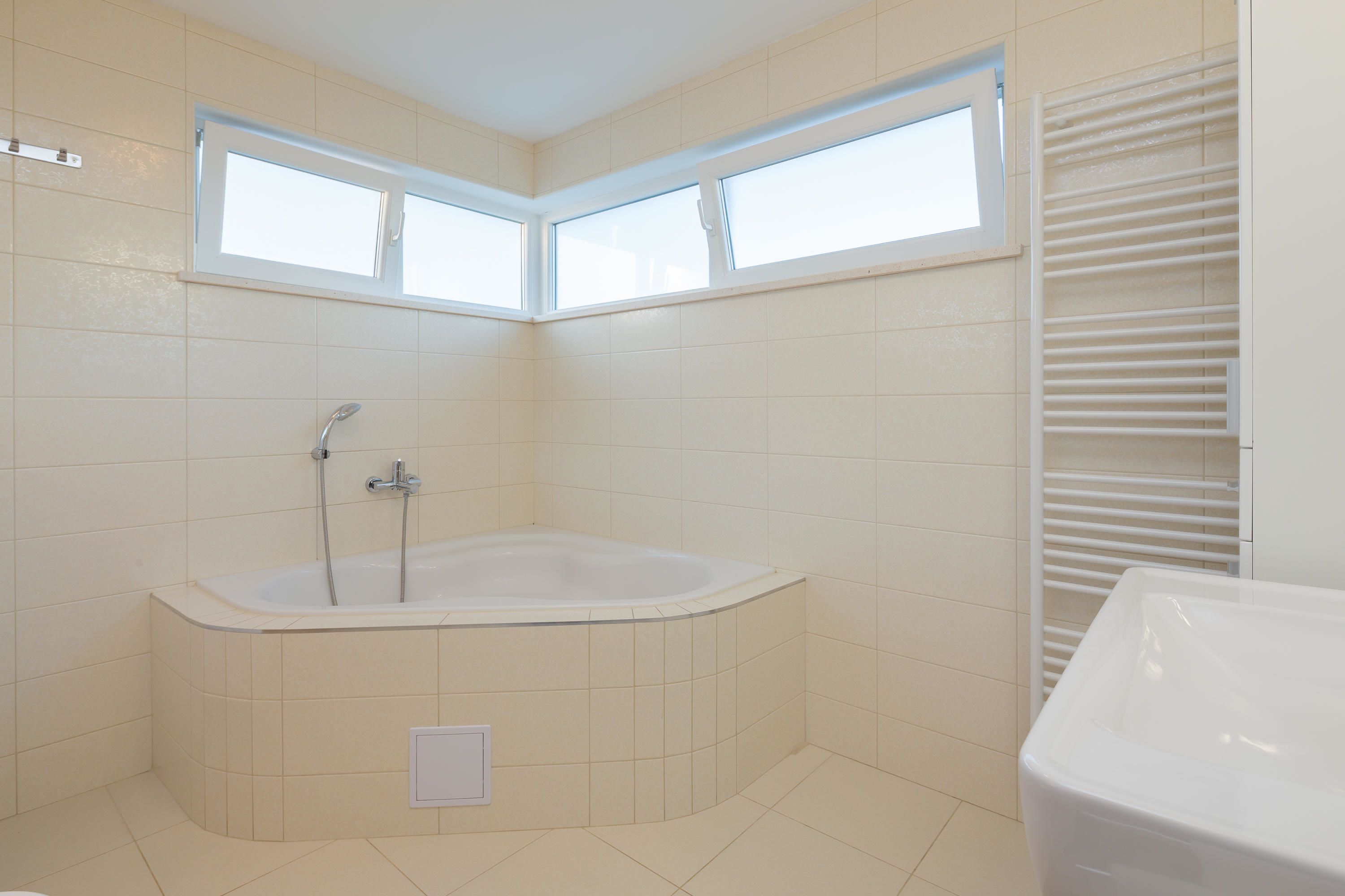 A modern bathroom with a freestanding bathtub, a shower, and a toilet. There are two windows providing natural light.