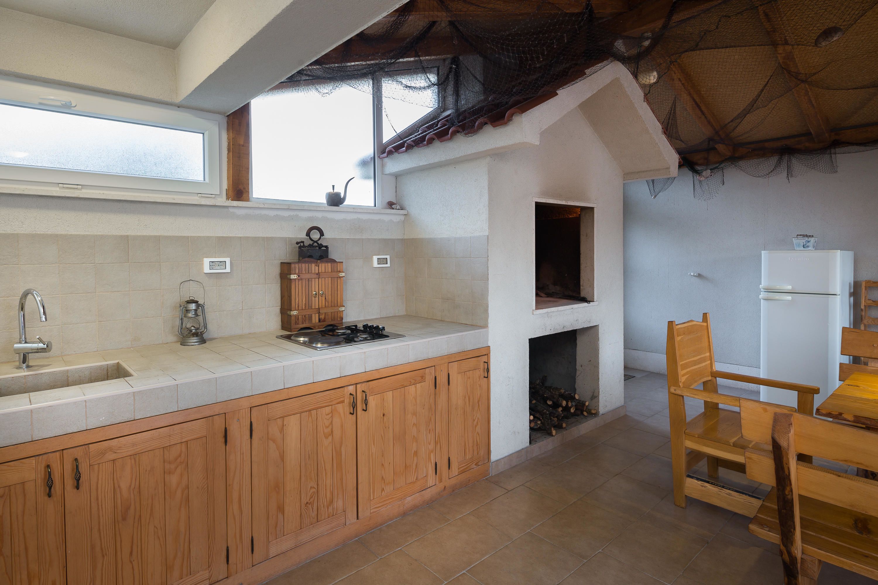 A kitchen with wooden cabinets, a sink, a stove, a window, and a ceiling with a thatched roof.