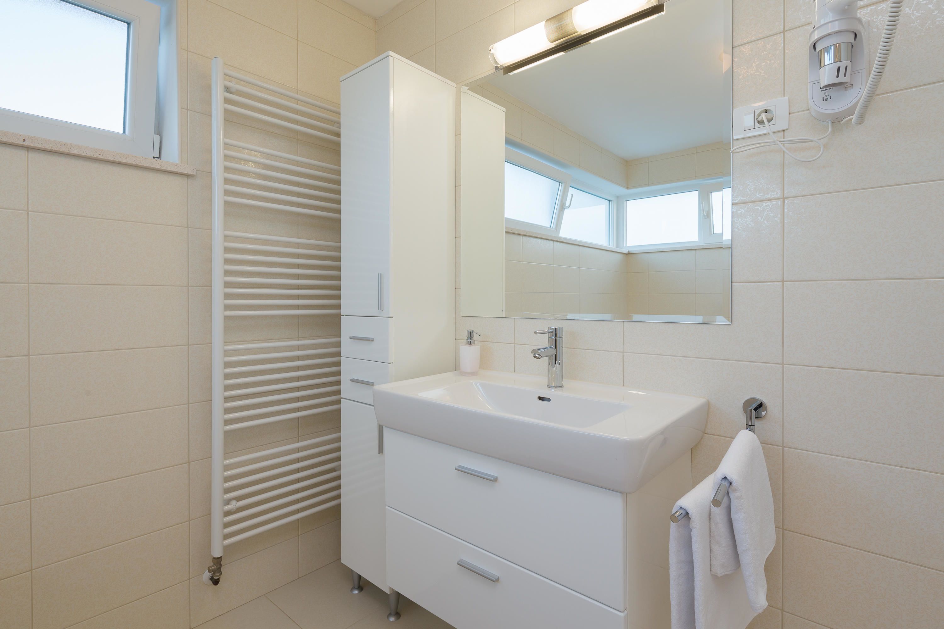 Ein modernes Badezimmer mit einem weißen Waschbecken, Spiegel und Schrank.