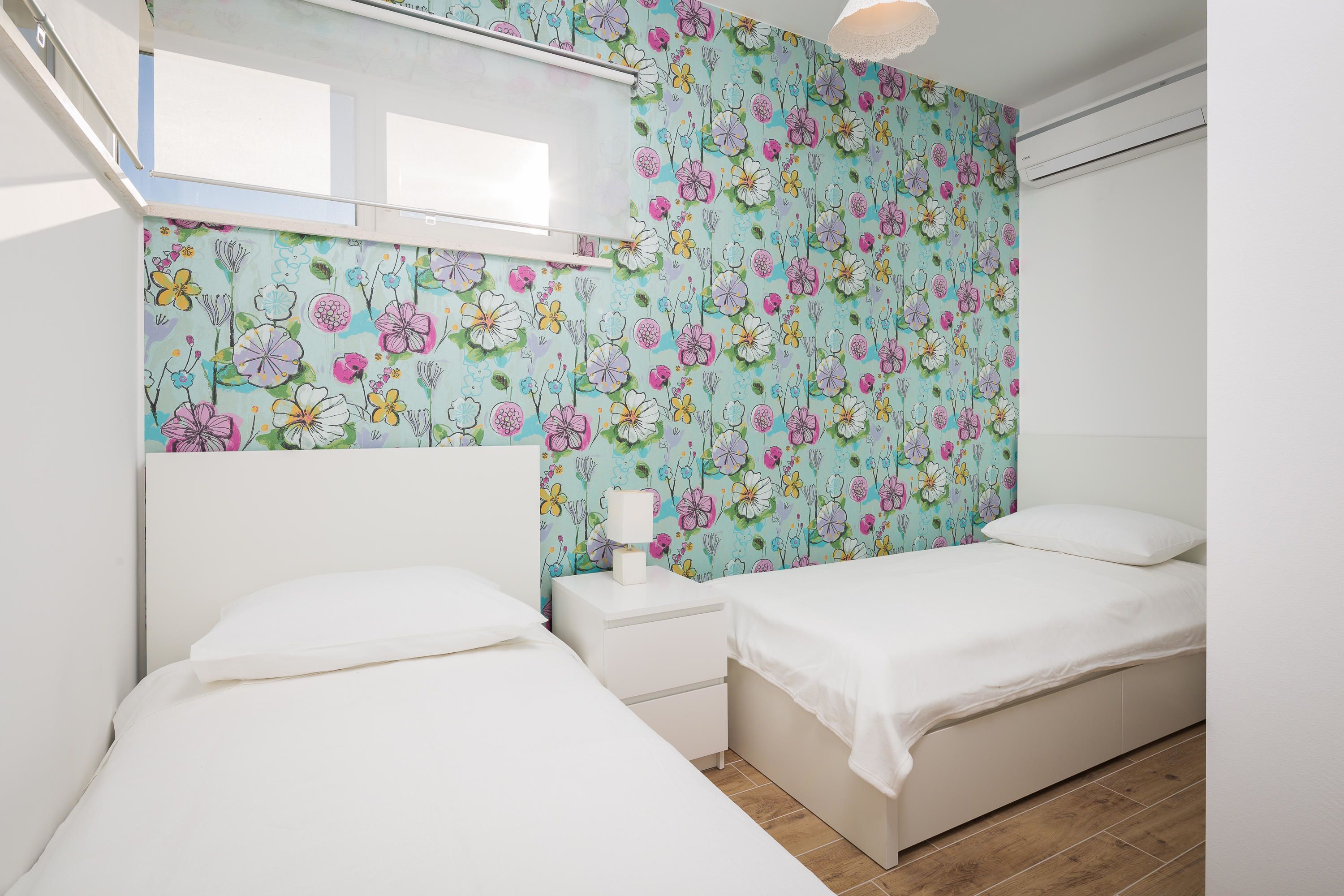 A bedroom with two beds, a nightstand, a window, and a floral wallpaper.