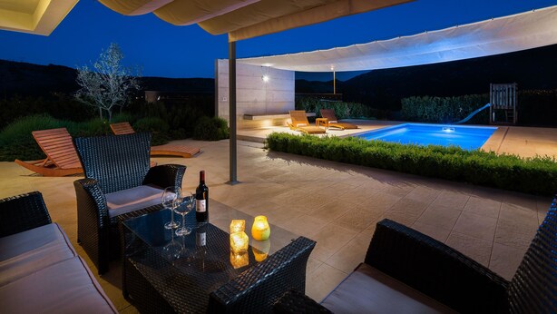 En udendørs terrasse med swimmingpool, liggestole og et bord med drikkevarer.