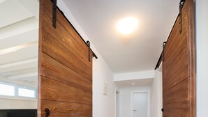 En gang med træskydedøre, flisegulv, en hvid dør i enden og en loftslampe.