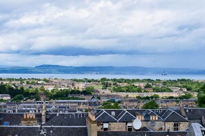 Un paisaje urbano costero con edificios históricos, un puerto y una plataforma petrolera distante.