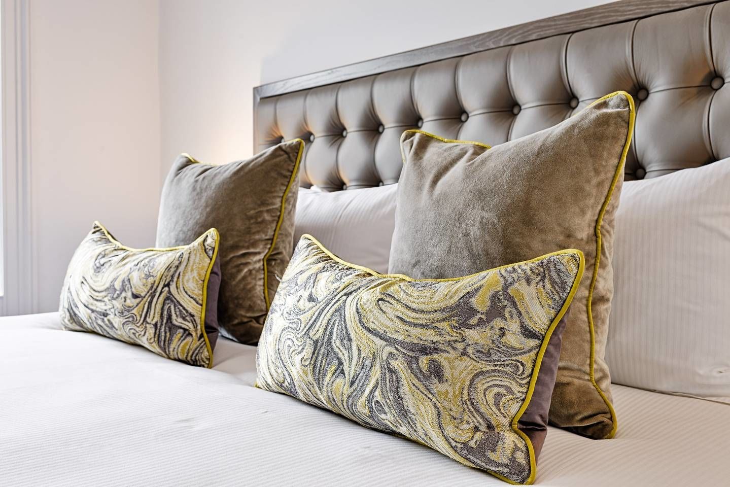 A bed with a tufted headboard, three pillows with a marbled pattern, and a plain white bedspread.