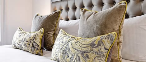 A bed with a tufted headboard, three pillows with a marbled pattern, and a plain white bedspread.
