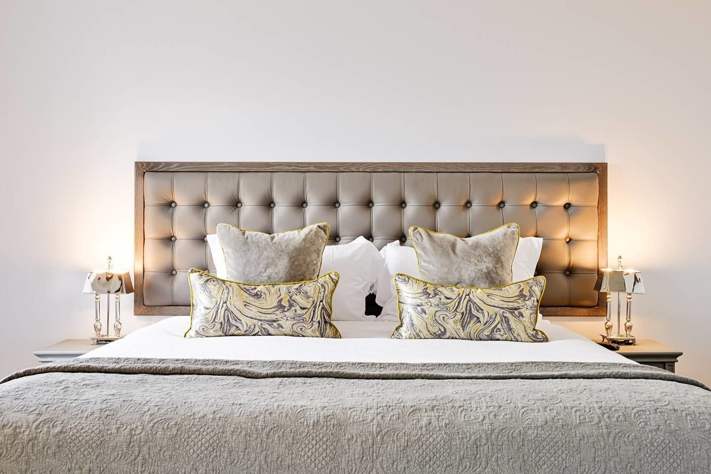 Een slaapkamer met een gestoffeerd hoofdeinde, twee nachtkastjes met lampen, en een bed met een bedovertrek met patroon.