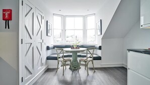 A kitchen with a bay window, a round table with chairs, and a fire blanket on the wall. - JOIVY Luxury George Street Apartments: Castle Suite (Edinburgh)