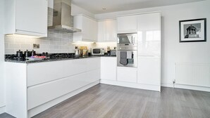 A modern kitchen with white cabinetry, a built-in oven, and a microwave. - JOIVY Luxury George Street Apartments: Castle Suite (Edinburgh)