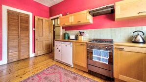 Une cuisine avec des meubles de rangement en bois, une cuisinière, un lave-vaisselle et un mur rose.