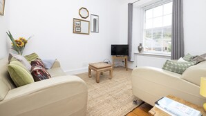 A living room with a beige sofa, a small wooden table, a TV, and a window with curtains. - JOIVY The Old Town Sugar House - Amazing Location (Edinburgh)